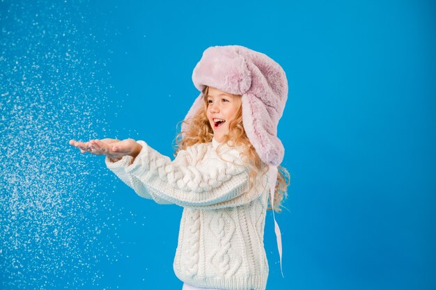 kleines blondes Mädchen in Winterkleidung bläst Schnee von ihren Händen