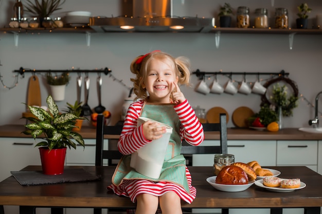 Kleines blondes Mädchen lächelt in der Küche, kocht einen Kuchen. Kind in der Küche. Bleib zuhause