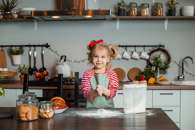 Kleines blondes Mädchen lächelt in der Küche, kocht einen Kuchen. Kind in der Küche. Bleib zuhause