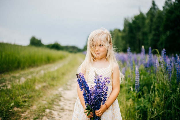 Kleines blondes Mädchen mit dem ausdrucksvollen Gesicht, das mit Blumenstrauß von Feldblumen in der Sommernatur aufwirft