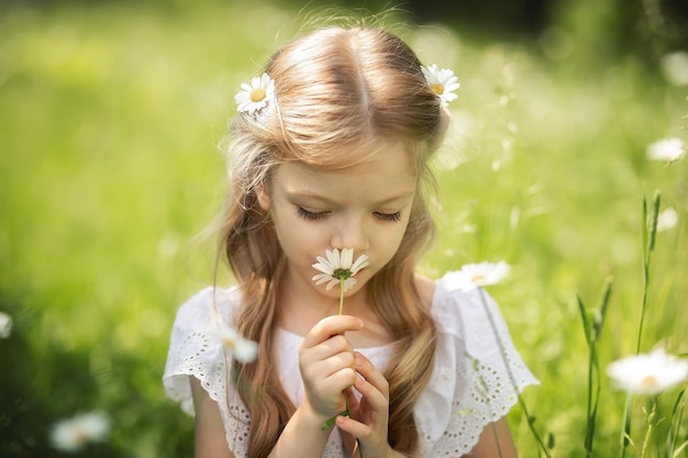 Kleines blondes Mädchen schnüffelt im Sommer an einem Haufen Gänseblümchen