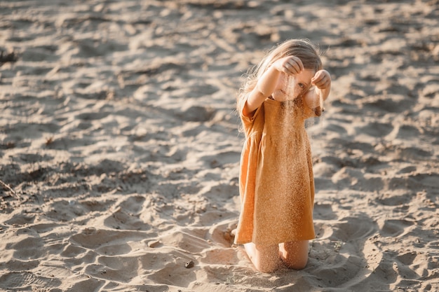 Kleines blondes Mädchen spielt auf dem Fluss im Sand gegen den Sonnenuntergangshimmel