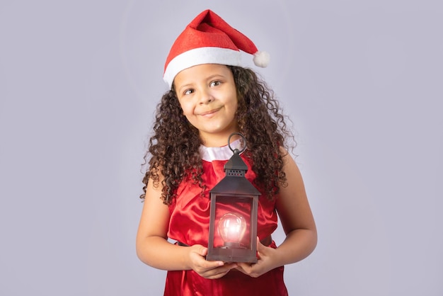 kleines brasilianisches Mädchen gekleidet mit Weihnachtskostüm, das Lampe hält