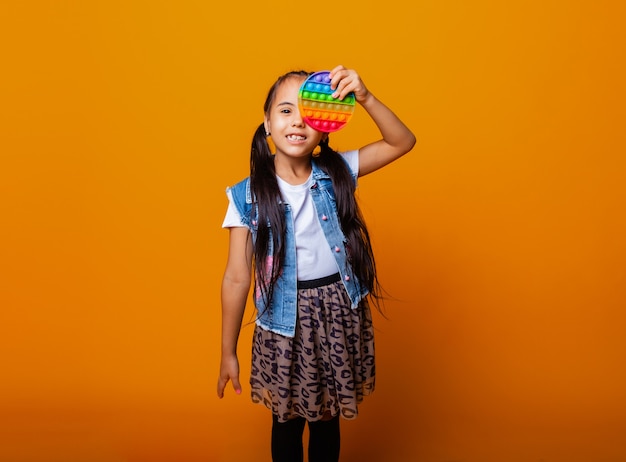Kleines brünettes Mädchen, das Pop-It-Antistress-Spielzeug auf gelbem Hintergrund mit Platz für Text hält