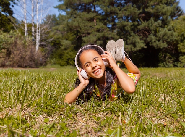 Kleines brünettes Mädchen hört Musik im Park auf dem Gras.