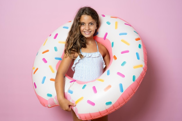 Kleines brünettes süßes Mädchen hält einen großen Gummiring auf rosa Hintergrund. Aktiver Urlaub mit der Familie am Strandpool. Emotionales Kind