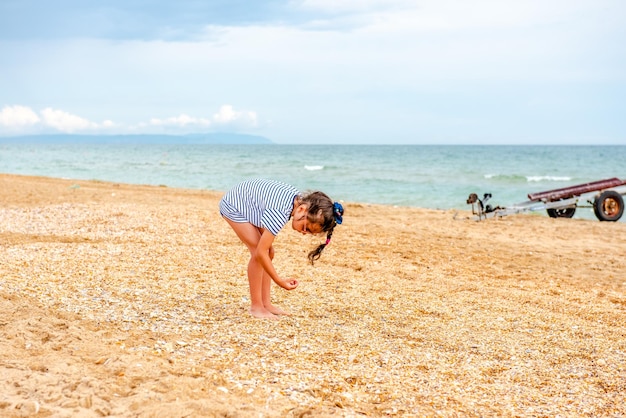 Kleines charmantes Mädchen in einem gestreiften T-Shirt spielt an einem sonnigen Tag im Urlaub glücklich am Strand