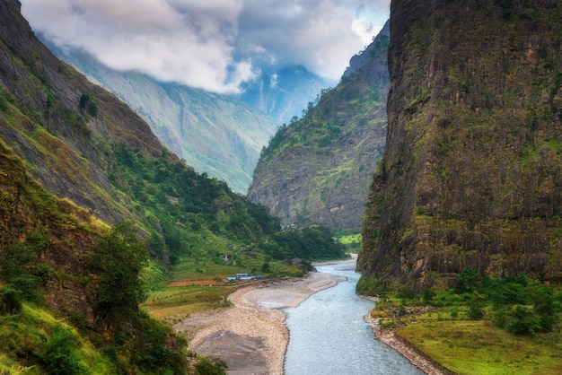 Kleines Dorf an der Flussküste im Himalaya-Gebirge. Schöne Flusshäuser, grüner Wald, Felsen, Himmel mit Wolken bei Sonnenuntergang. Sommer in Nepal. Bergschlucht. Wandern in der Naturlandschaft des Himalaya