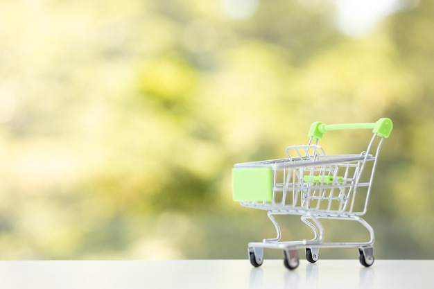 Kleines Einkaufswagenspielzeug auf grünem Sommerhintergrund Leerer Einkaufswagen