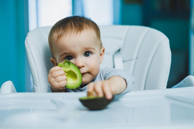 Kleines entzückendes Baby, das Avocado Vitamin und gesunde Ernährung für kleine Kinder isst Porträt eines schönen Kindes von 8 Monaten