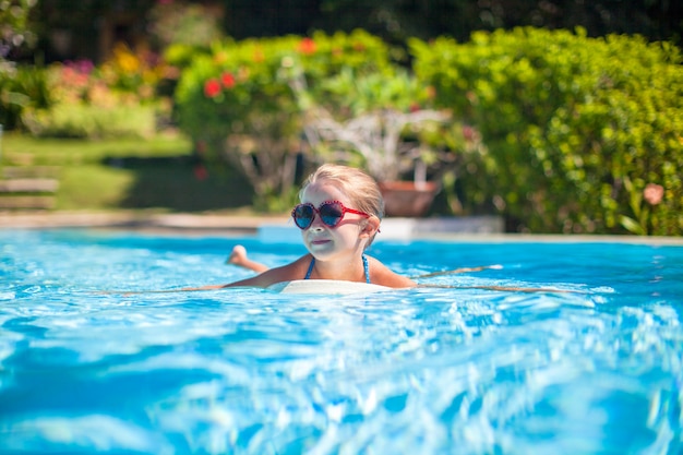 Kleines entzückendes glückliches Mädchen schwimmt im Swimmingpool