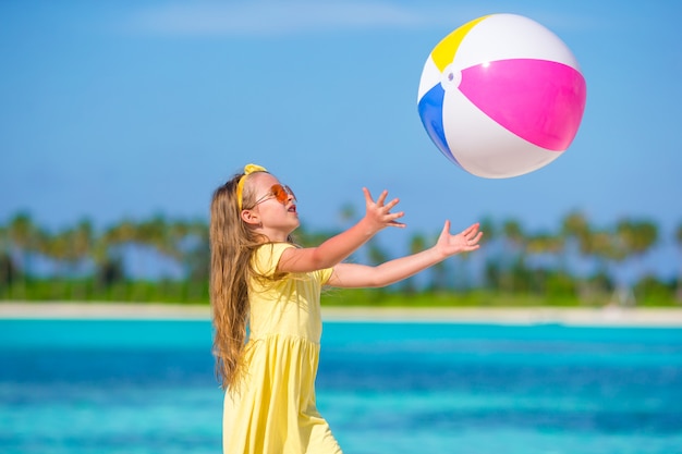 Kleines entzückendes Mädchen, das auf Strand mit Ball spielt