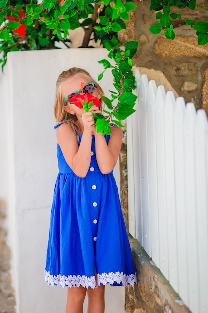 Kleines entzückendes Mädchen, das draußen bunte Blumen auf griechischen Straßen riecht