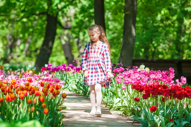 Kleines entzückendes Mädchen in blühendem Tulpengarten. Warmer Frühlingstag draußen