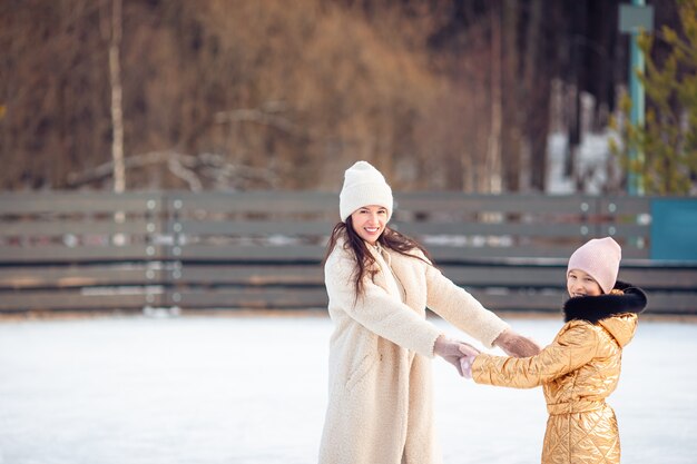 Kleines entzückendes Mädchen mit ihrer Mutter, die auf Eisbahn eisläuft