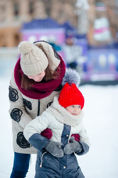 Kleines entzückendes Mädchen mit ihrer Mutter, die auf Eisbahn eisläuft