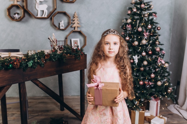 Kleines fröhliches Mädchen in der Weihnachtsdekoration mit Tee am gemütlichen Haus mit bunten Neujahrslichtern