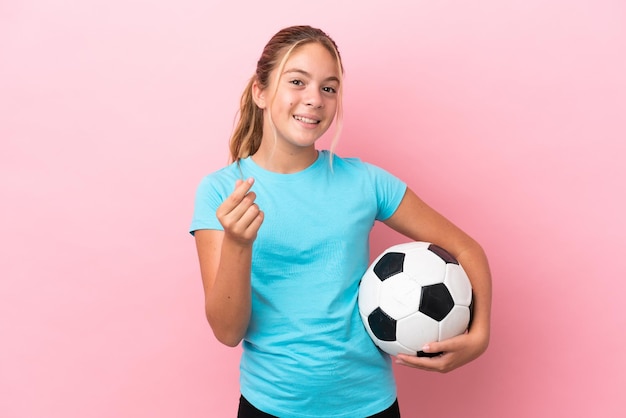 Kleines Fußballspielermädchen lokalisiert auf rosa Hintergrund, der Geldgeste macht