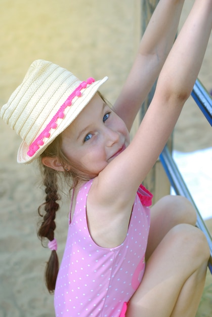 Kleines gir im Strohhut, der am Spielplatz spielt.