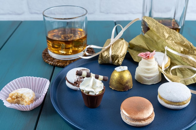 Kleines Glas Schokolade mit Schlagsahne neben Macarons Walnuss-Cameo-Trüffelflasche und Glas Whiskey