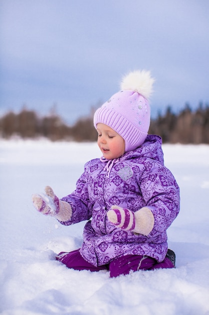 Kleines glückliches Mädchen, das Spaß auf dem Schnee am sonnigen Tag des Winters hat