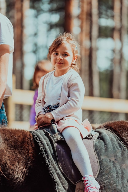 Kleines glückliches Mädchen, das Spaß im Park hat, während es kleine Pferde reitet.