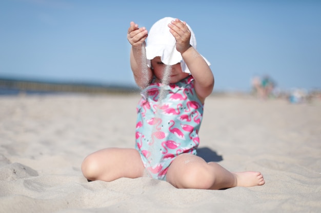 Kleines glückliches Mädchen gießt weißen Sand am Strand, genießt Sommer, Urlaub