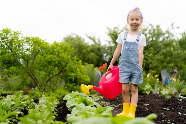 Foto kleines glückliches mädchen im garten mit einer gießkanne das konzept der gartenarbeit und des anbaus von pflanzen ein kind kümmert sich um gemüse