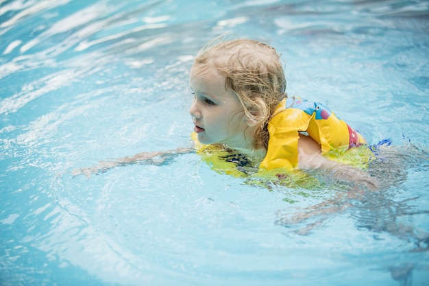 Kleines glückliches Mädchen lächelt und schwimmt im Außenpool schön und glücklich