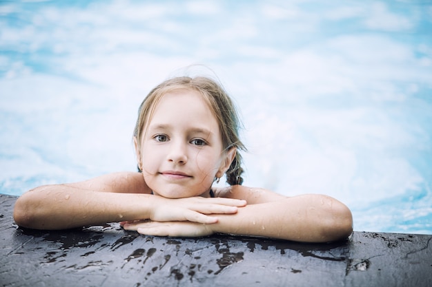 Kleines glückliches Mädchen lächelt und schwimmt im Außenpool schön und glücklich