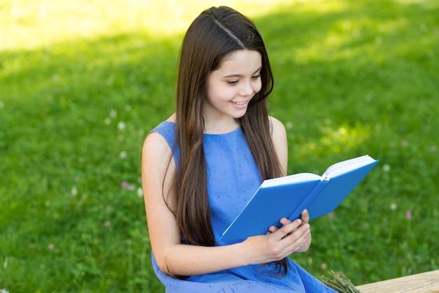 Kleines glückliches Mädchen liest Buch im Freien sonniger Tag cooles Story-Konzept