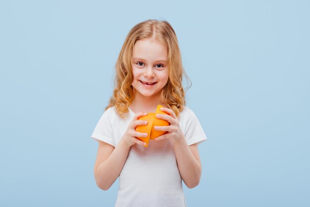 Kleines glückliches Mädchen mit einer Orange in der Hand