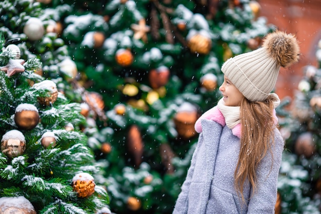 Kleines glückliches Mädchen nahe Tannenbaumniederlassung im Schnee für neues Jahr.