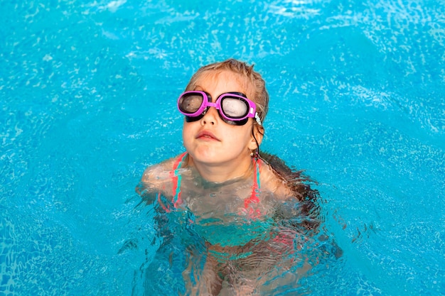 Kleines glückliches Mädchen schwimmt im Pool. Sommerferien. Mädchen in Badeanzug und Schwimmbrille.