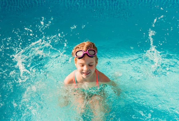 Kleines glückliches Mädchen schwimmt im Pool. Sommerferien. Mädchen in Badeanzug und Schwimmbrille.