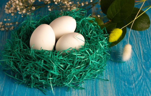 Kleines grünes Nest mit weißen Öko-Eiern mit Blumen auf hellblauem Holz