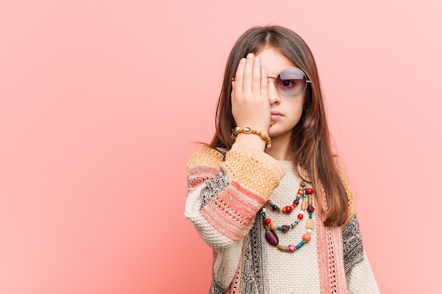 Kleines hippie-mädchen, das spaß hat, das halbe gesicht mit handfläche bedeckend.