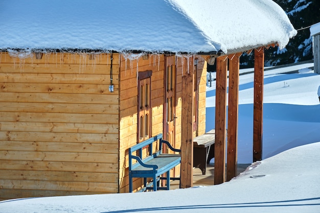 Kleines Holzhaus bedeckt mit frisch gefallenem Schnee, umgeben von hohen Kiefern in den Winterbergen.