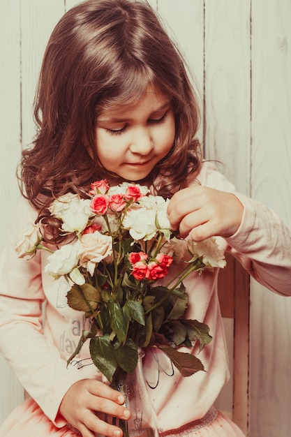 Kleines hübsches Mädchen in Rosa hält den Rosenstrauß. Schließen Sie die Blumen und das Gesicht