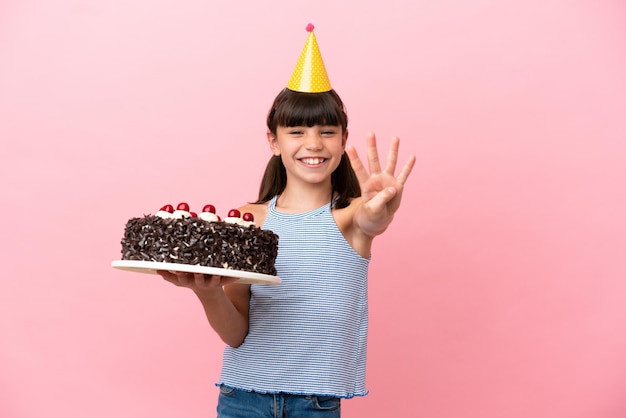 Kleines kaukasisches Kind, das Geburtstagstorte isoliert auf rosafarbenem Hintergrund hält, glücklich und vier mit den Fingern zählend