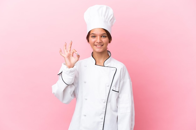 Kleines kaukasisches Kochmädchen isoliert auf rosa Hintergrund, das mit den Fingern ein Ok-Zeichen zeigt