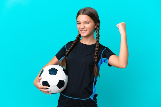 Kleines kaukasisches Mädchen auf blauem Hintergrund mit Fußball, das einen Sieg feiert