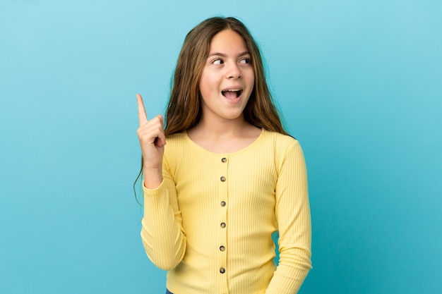 Kleines kaukasisches Mädchen, das auf blauem Hintergrund isoliert ist und beabsichtigt, die Lösung zu realisieren, während es einen Finger hochhebt