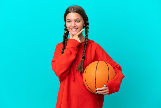 Foto kleines kaukasisches mädchen, das basketball lokalisiert auf blauem hintergrund glücklich und lächelnd spielt