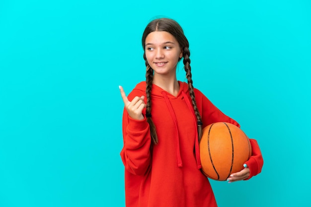 Kleines kaukasisches Mädchen, das Basketball spielt, isoliert auf blauem Hintergrund, das auf eine großartige Idee zeigt