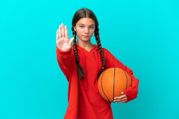 Kleines kaukasisches Mädchen, das Basketball spielt, isoliert auf blauem Hintergrund und Stoppgeste macht