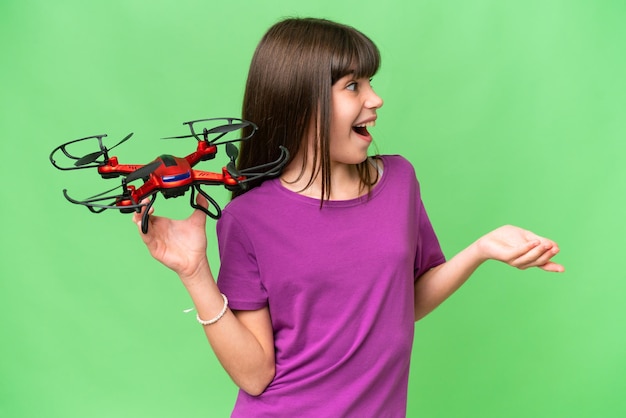 Kleines kaukasisches Mädchen, das eine Drohne über isoliertem Hintergrund mit überraschendem Gesichtsausdruck hält