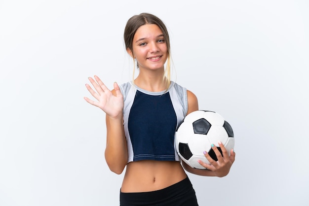 Kleines kaukasisches Mädchen, das Fußball spielt, isoliert auf weißem Hintergrund, salutiert mit der Hand mit glücklichem Ausdruck