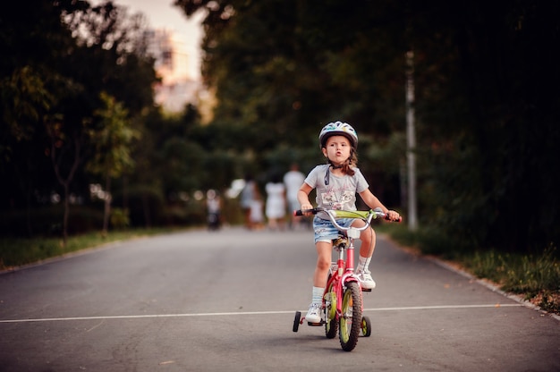 Kleines kaukasisches Mädchen, das lernt, ein Fahrrad im Kinderhelm im Park zu fahren