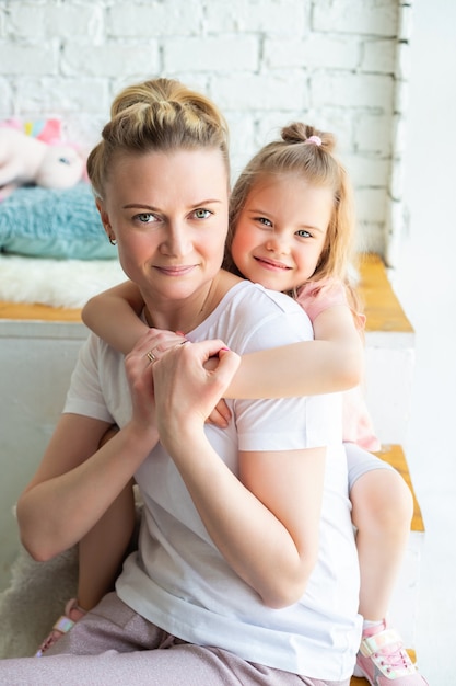 kleines kaukasisches Mädchen, das mit der Mutter sitzt, die auf der Fensterbank sitzt und sich umarmt